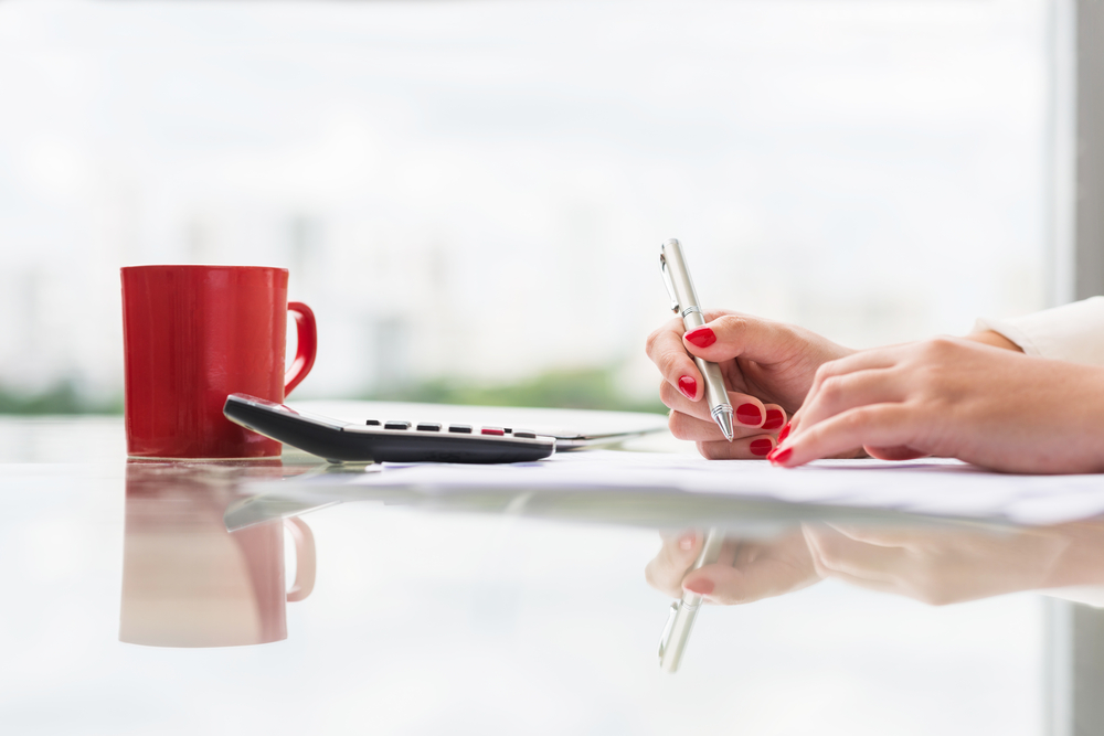 Female computing tax with a calculator and red mug on the table