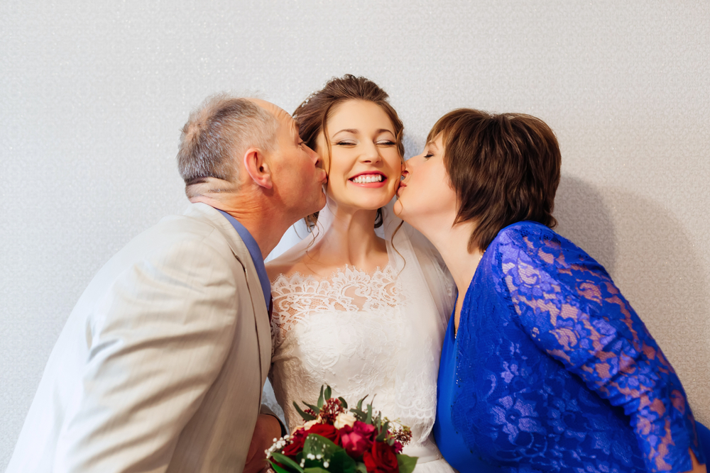 Parents kissing their smiling daughter on her civil wedding day