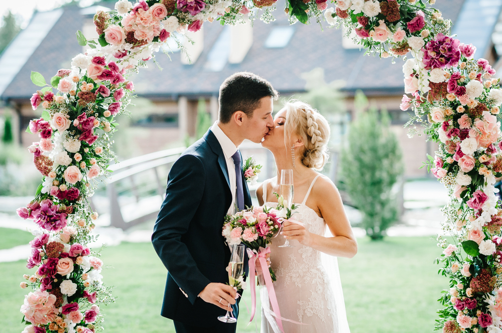 The bride holding a bouquet and groom holding a glass of wine kissing