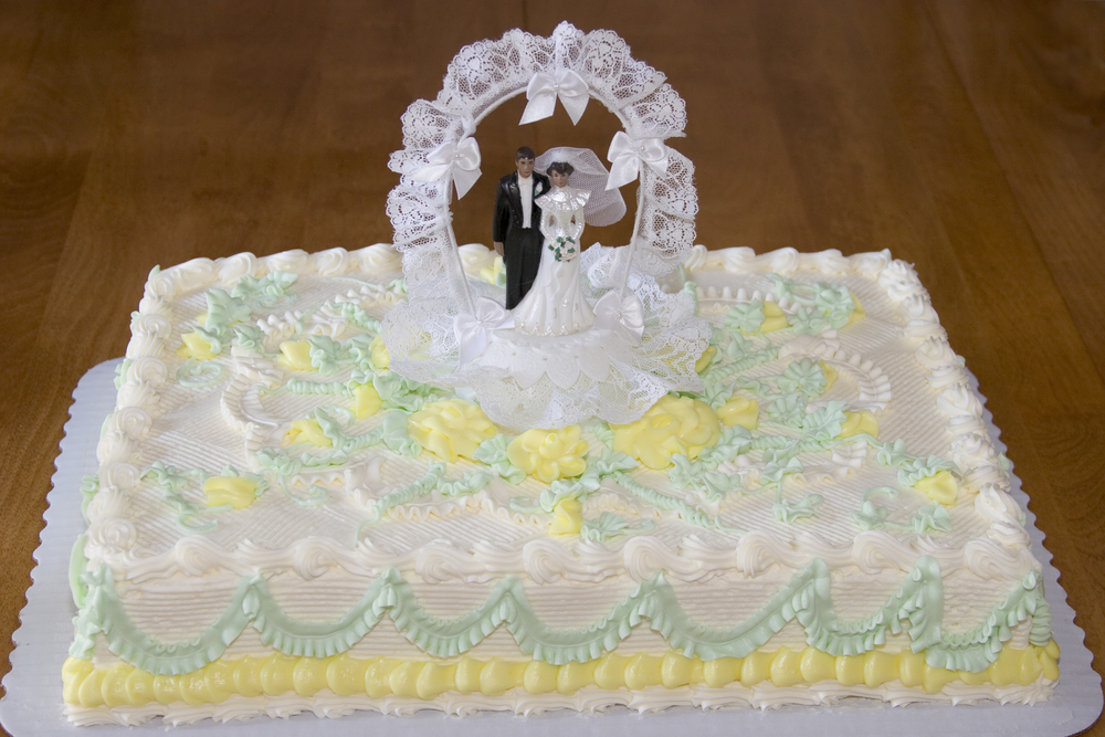 White Sheet wedding cake with bride and groom figurines on wooden table