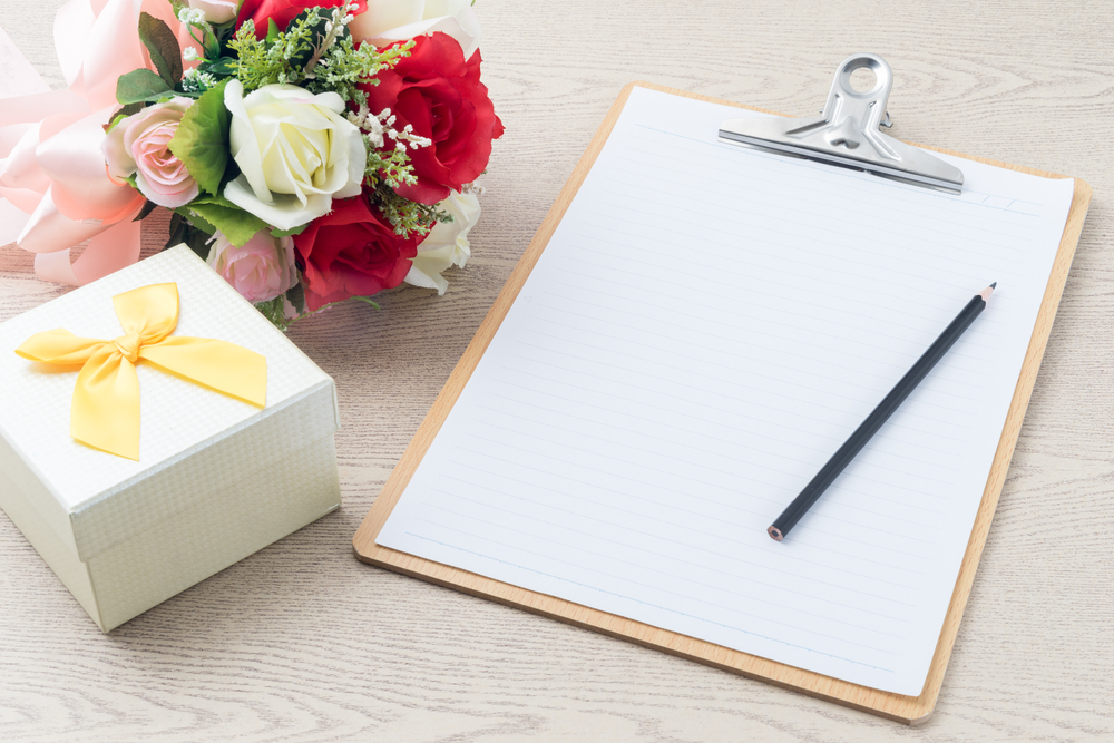 a planning paper attached to wooden clipboard with pencil, bouquet, and gift box