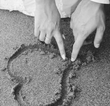 man and woman draw heart on sand