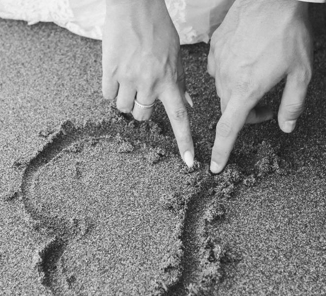 man and woman draw heart on sand