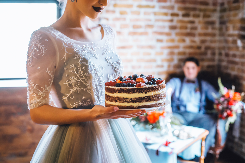 naked type of wedding cake with berries in hands of a bride