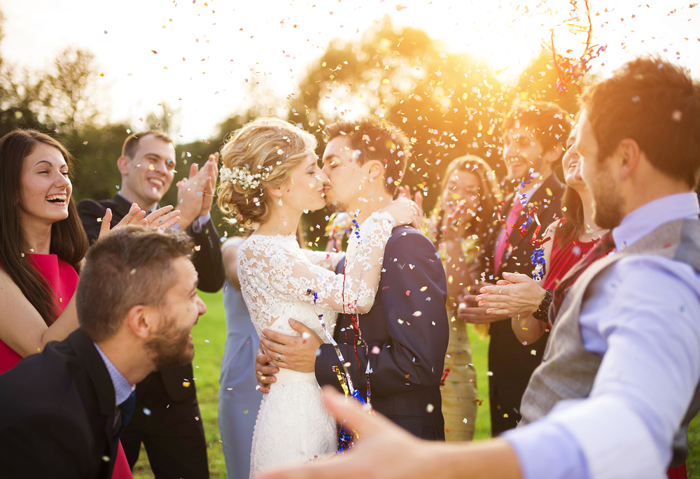 newlywed couple kissing and their friends at an outdoor wedding party