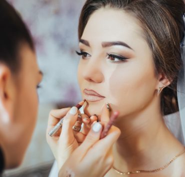 woman putting lip outliner on bride's lips