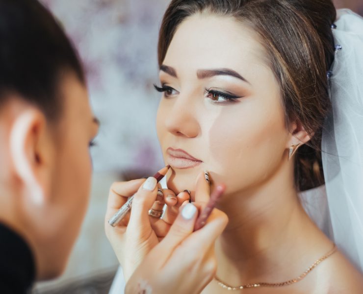 woman putting lip outliner on bride's lips
