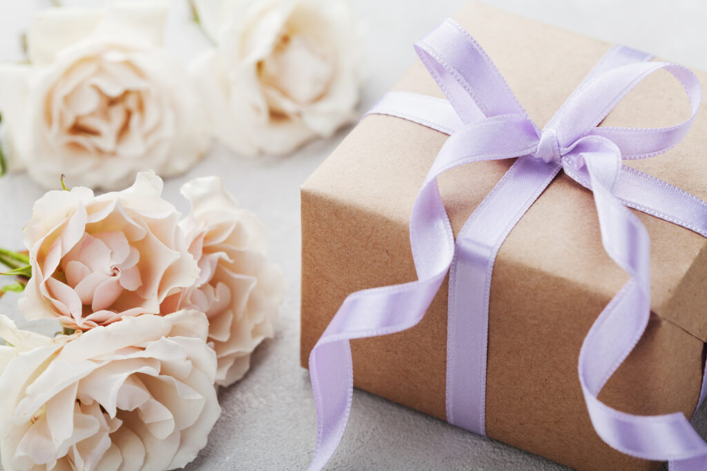 a gift with purple ribbon beside white roses