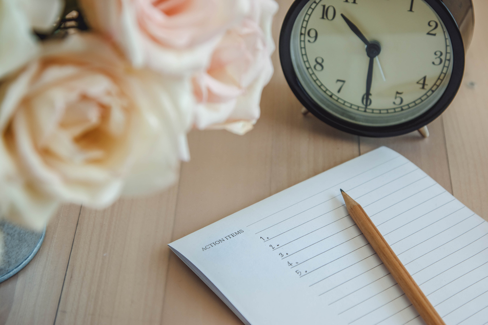 Action Items list on notebook with pencil, vintage clock, and roses, on wooden table