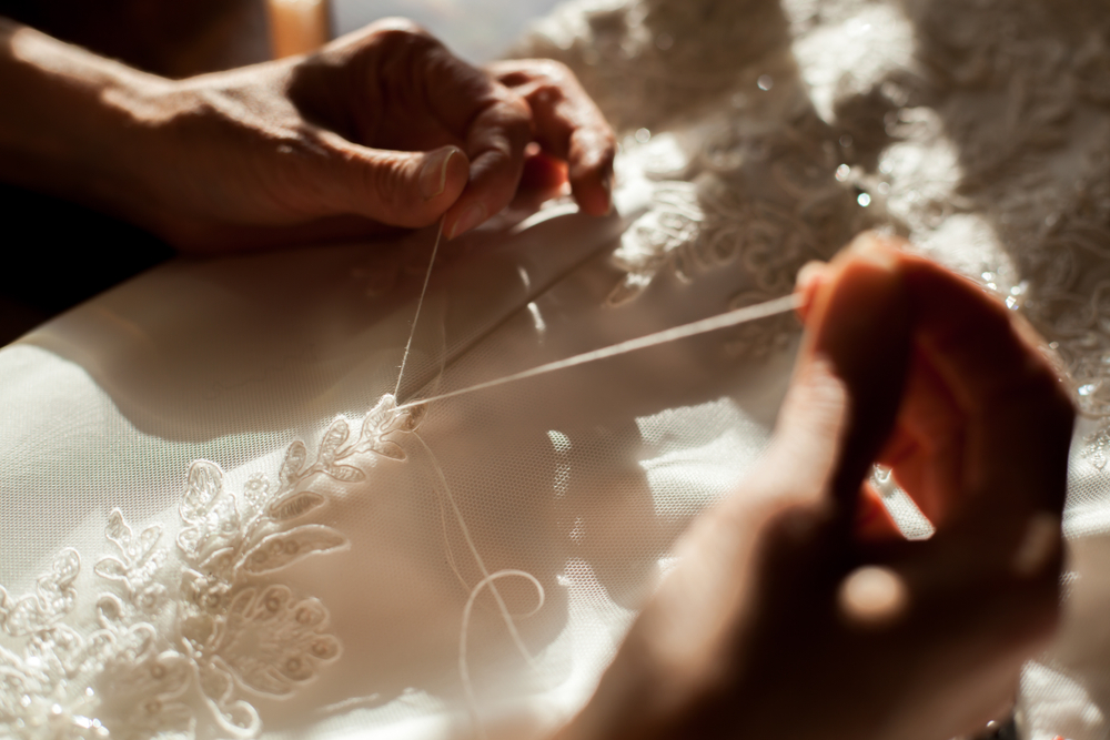 a tailor embroiders lace details on a wedding dress