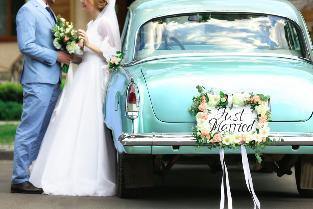 bride and groom next to the wedding car that has a plate with text that says Just Married