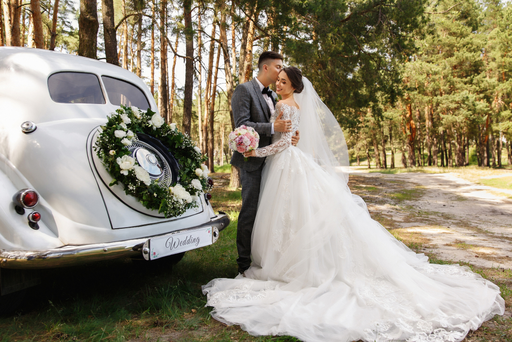 groom kissing the bride with a wedding car at their side