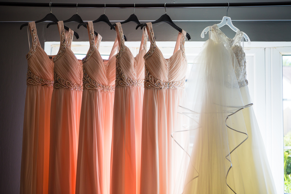 gown of the bride along with the gowns of the bridesmaids hanged in a clothing rack