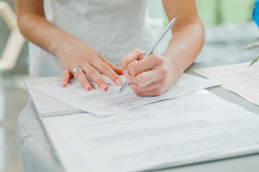 A bride wearing white dress and signing marriage documents