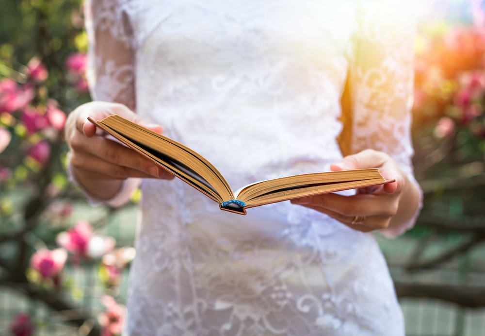 A woman on white dress reading a book and in a garden