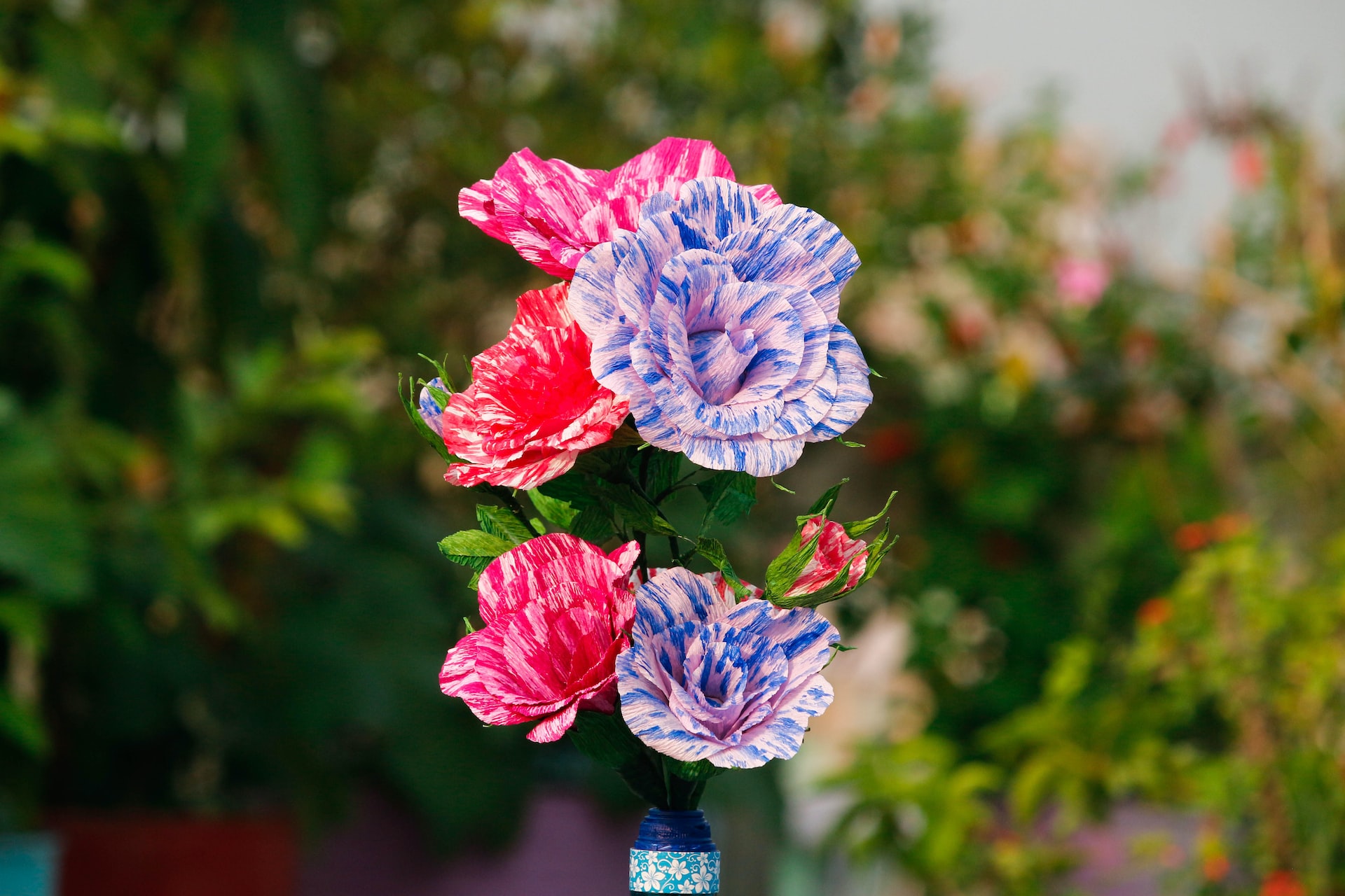 Colorful handmade origami paper flowers in small blue glass vase