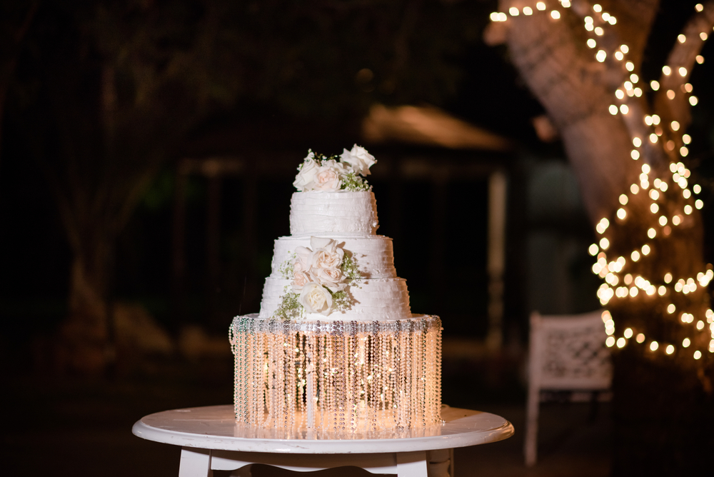 Three tiered wedding cake with crystal base displayed in an outdoor reception at night