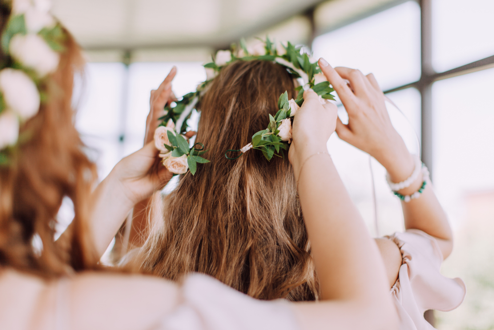 a bridesmaid putting a flower wreath on another bridesmaid's head