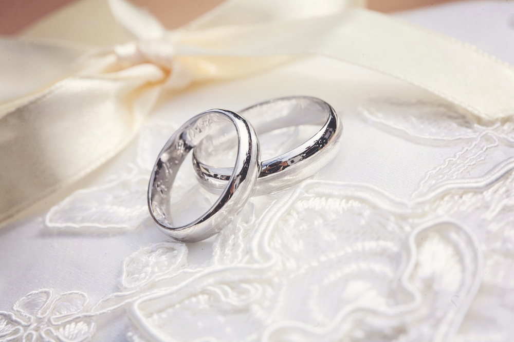 silver wedding rings on top of white floral cloth background