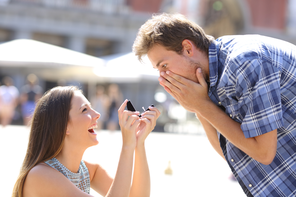 a smiling woman proposing to her surprised boyfriend on street