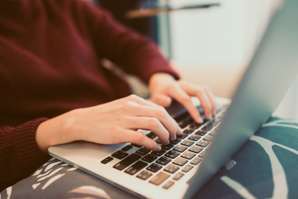 woman wearing red sweater is typing on laptop