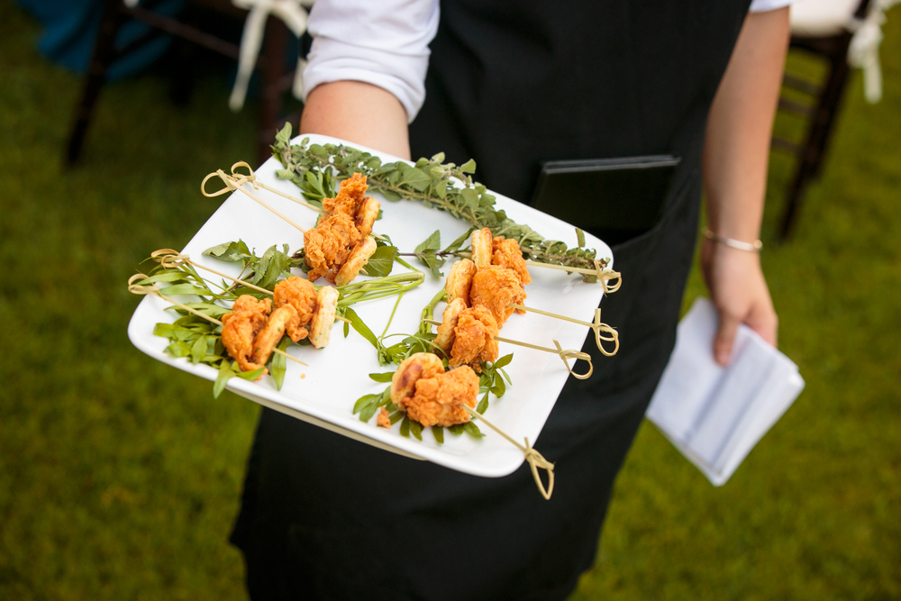 a waiter holding a plate of mini fried chicken and waffles on wedding day