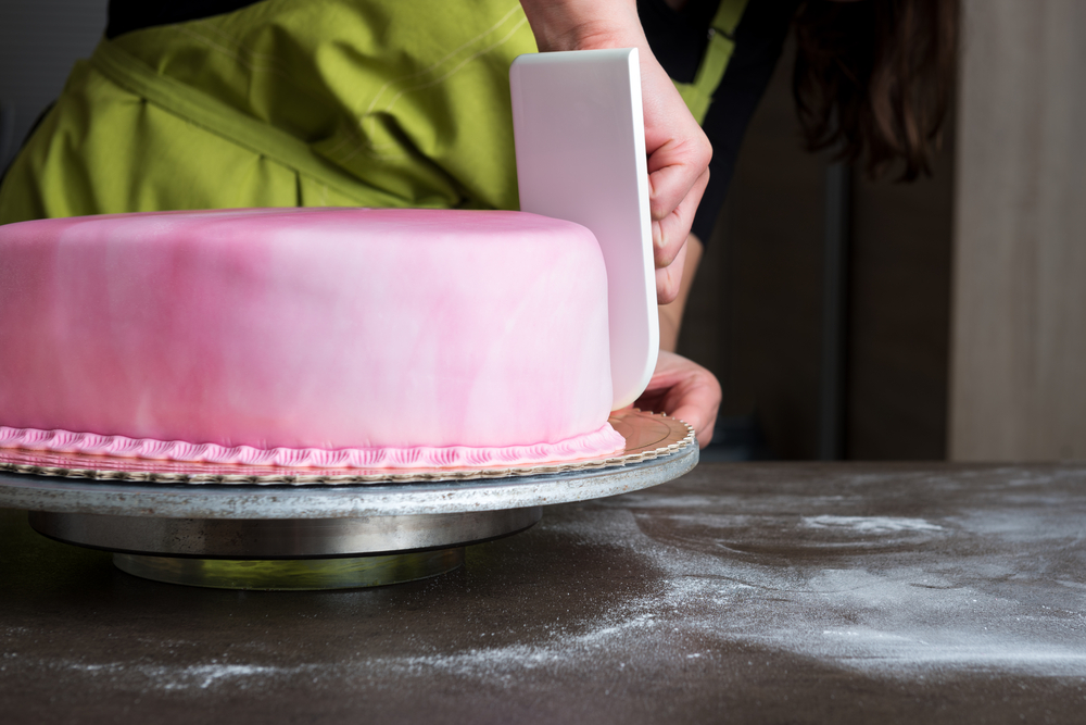 female baker shaping pink fondant frosting on cake