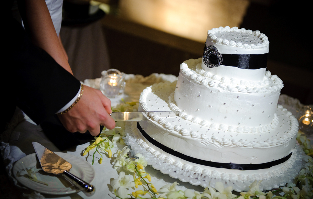 hands of newlywed cutting white frosted wedding cake