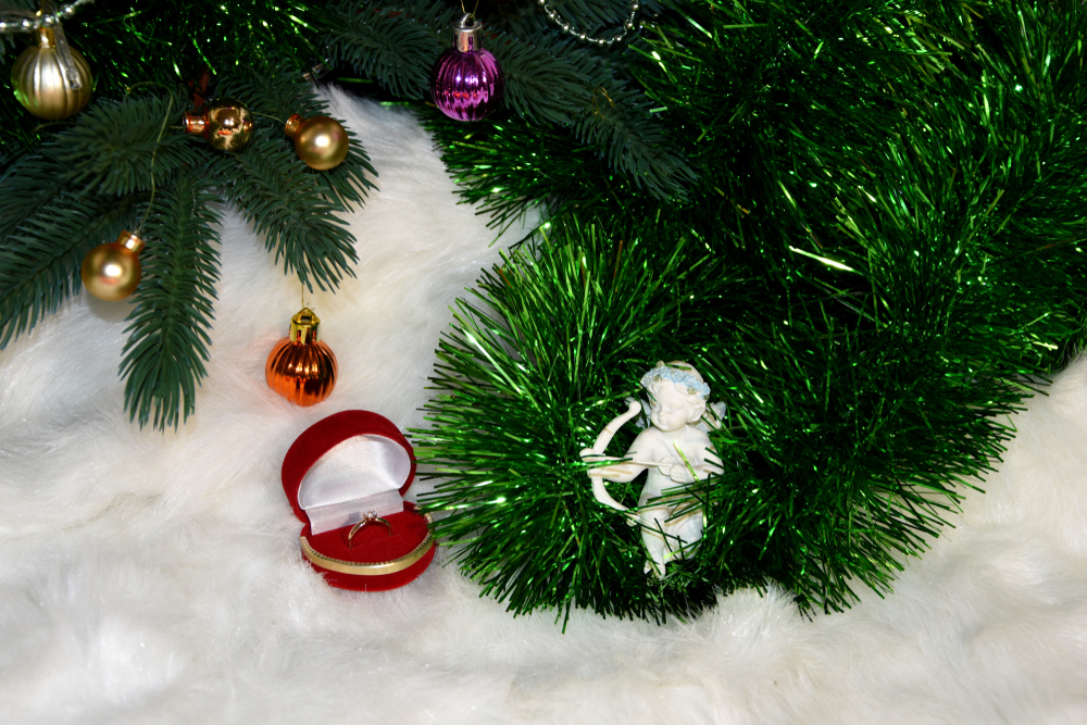 A figurine of Cupid aiming from a bow directly into a ring under a Christmas tree