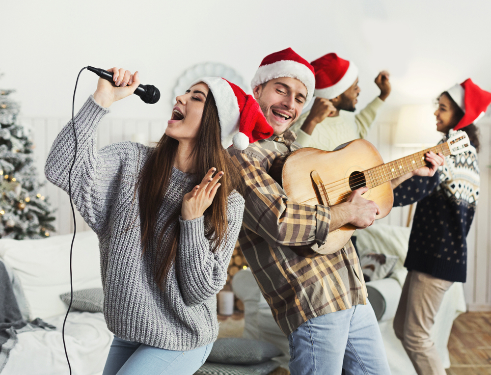 Happy couple playing on guitar and singing Christmas song in house with friends
