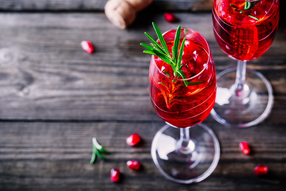 Pomegranate champagne mimosa cocktail with rosemary in glasses on wooden background