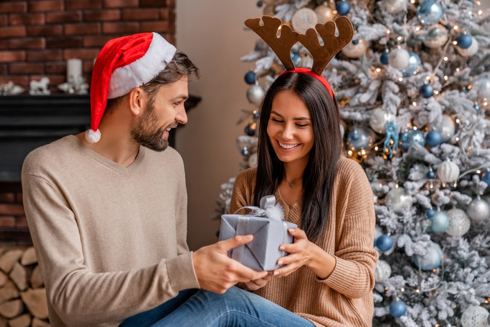 husband handing a gray gift box to his wife on Christmas