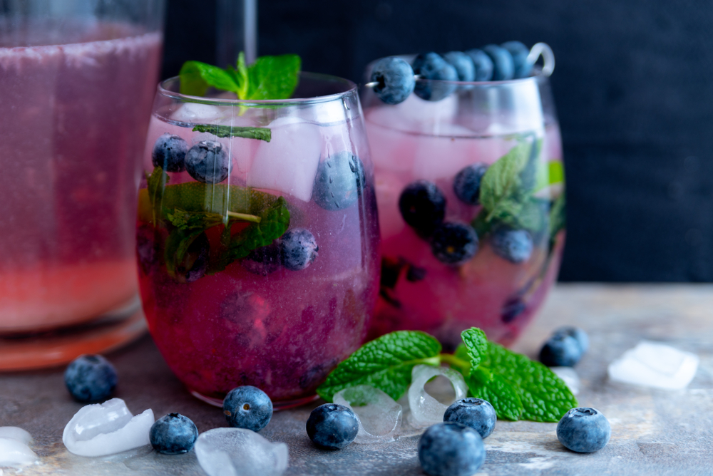 two blueberry mojitos with blueberries and lemonade pitcher image in dark moody style