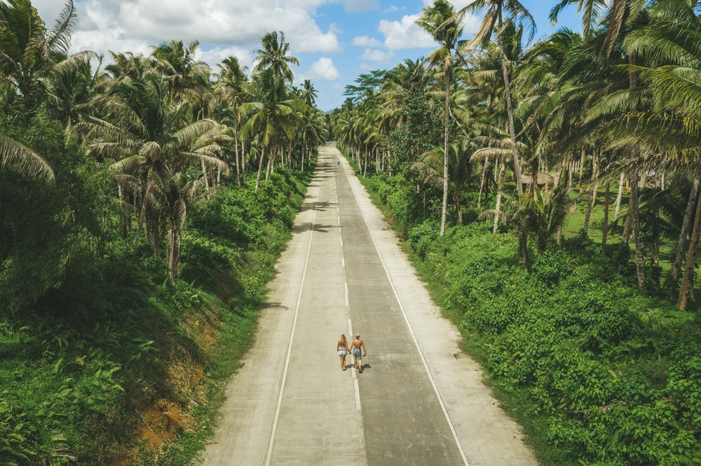 Aerial drone view of a couple on the road with palm trees in Siargao, Philippines