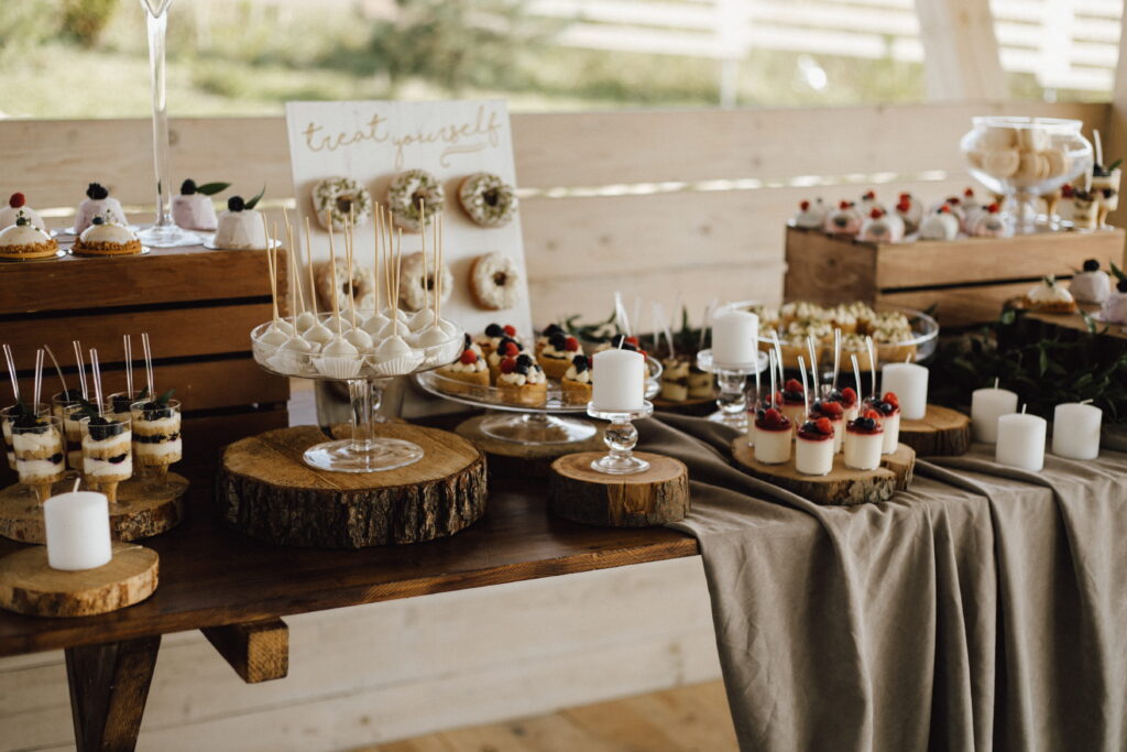 Rustic dessert table featuring cake pops, mini parfait cups, donuts, and white candles on wooden slabs