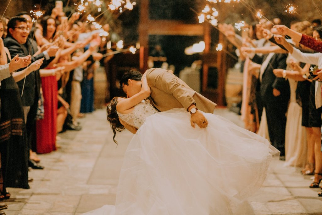 happy newlywed kissing in front of guest holding sparkling sticks 