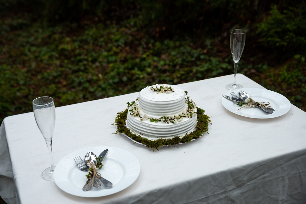 minimalistic white wedding cake, utensils, glasses, and plates on table