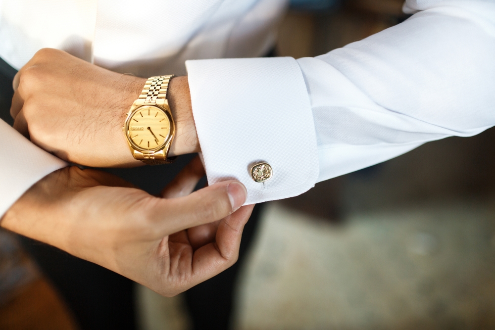 A groom fastens his cufflink and wearing borrowed vintage watch at the wedding 
