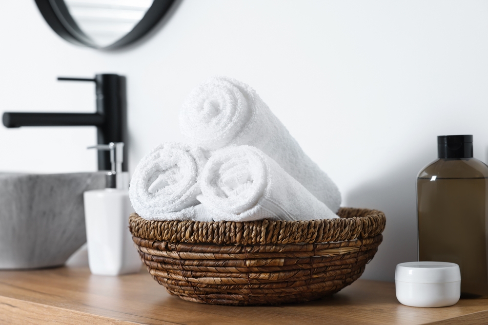 Wicker bowl with rolled bath towels on wooden table in bathroom