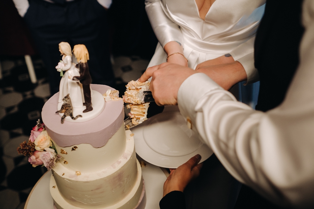 bride and groom slicing their wedding cake with figures at the top