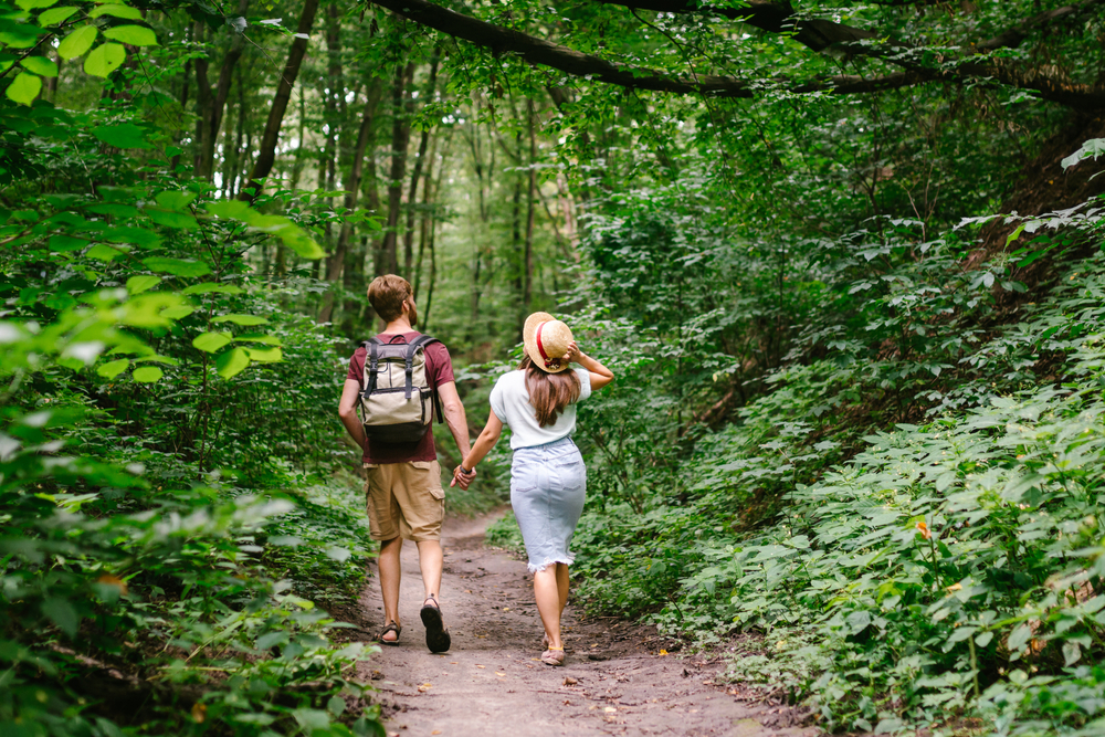 couple walking in the forest while the man is wearing a picnic backpack