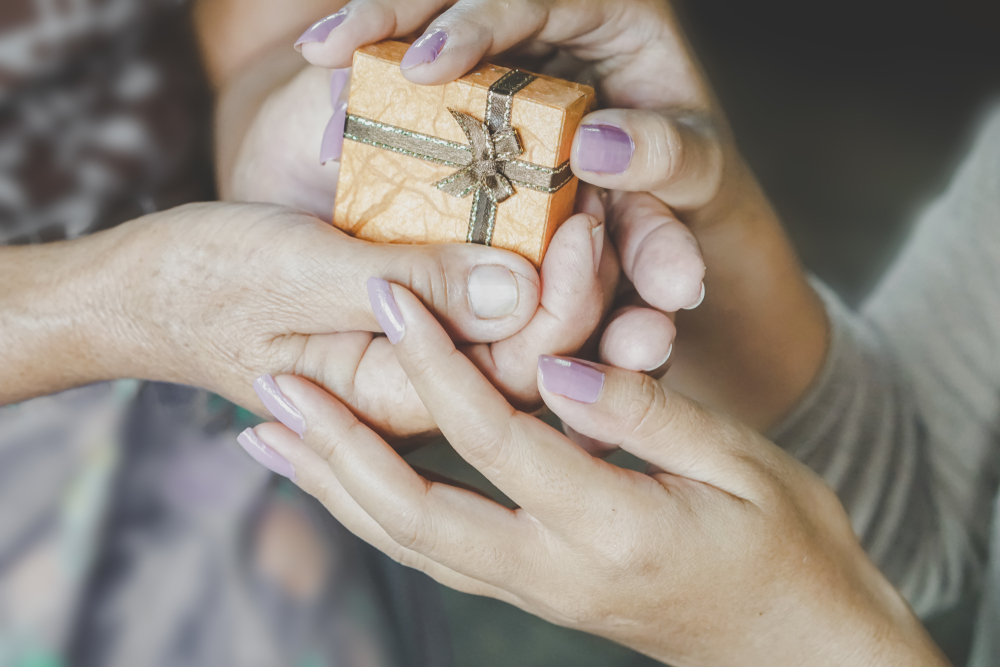 hands of old person handing over a gift to a young woman's hands