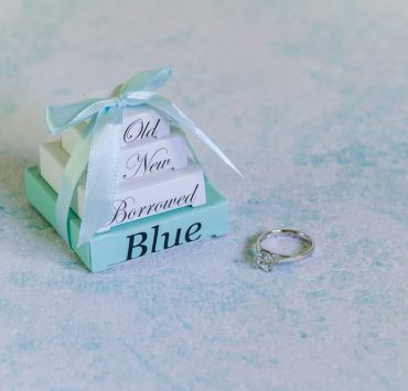 old, new, borrowed, and blue labeled small boxes stacked and tied with a ribbon and beside a ring