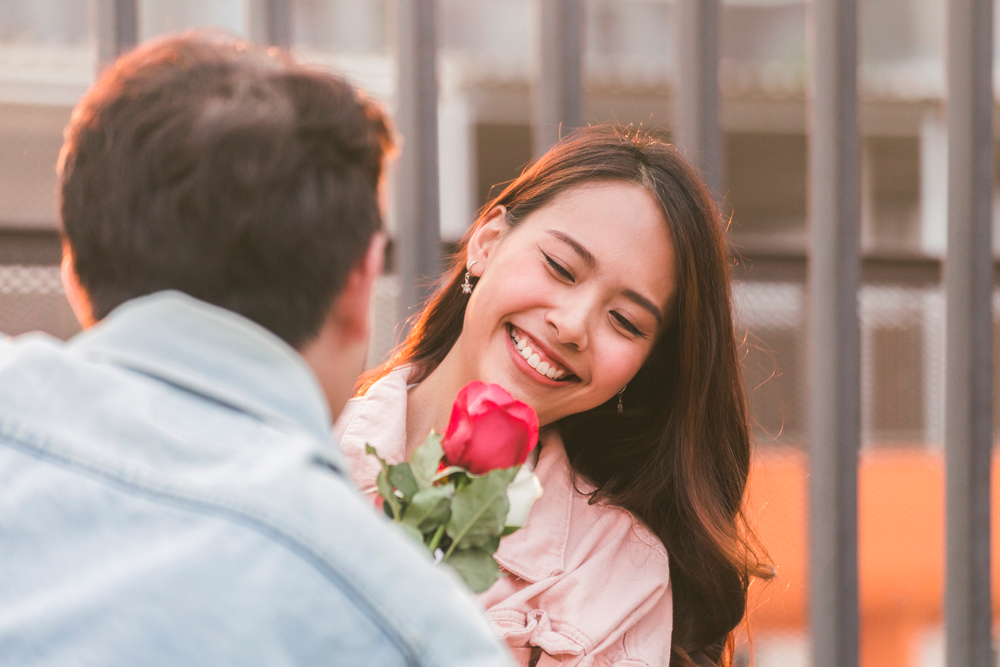 woman smilling as she receives a red rose from a man