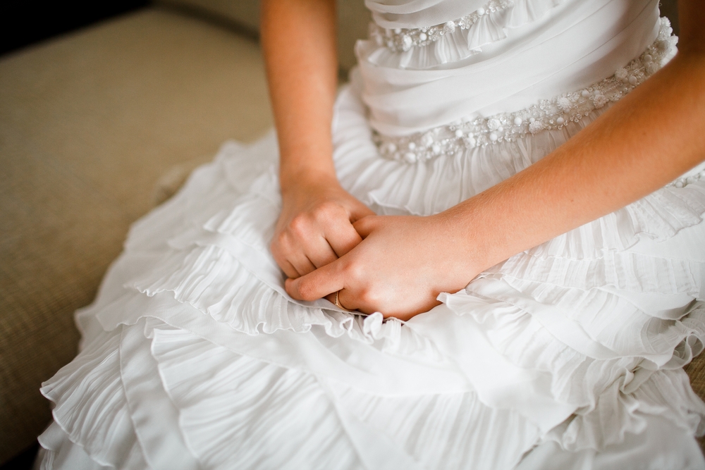 hands of nervous bride on white wedding dress