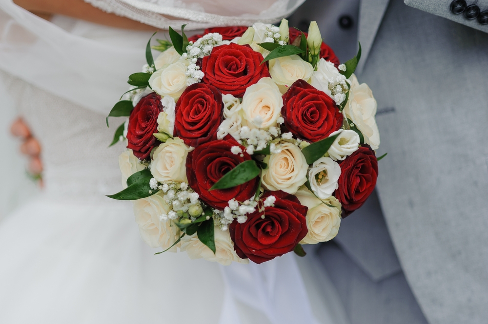 red and white roses bouquet between bride and groom
