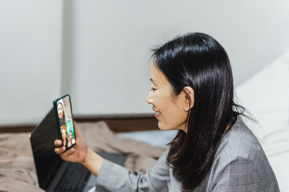 woman sit on bed at home video calling friends on smartphone
