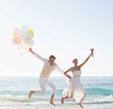 two newly weds jumping on the beach