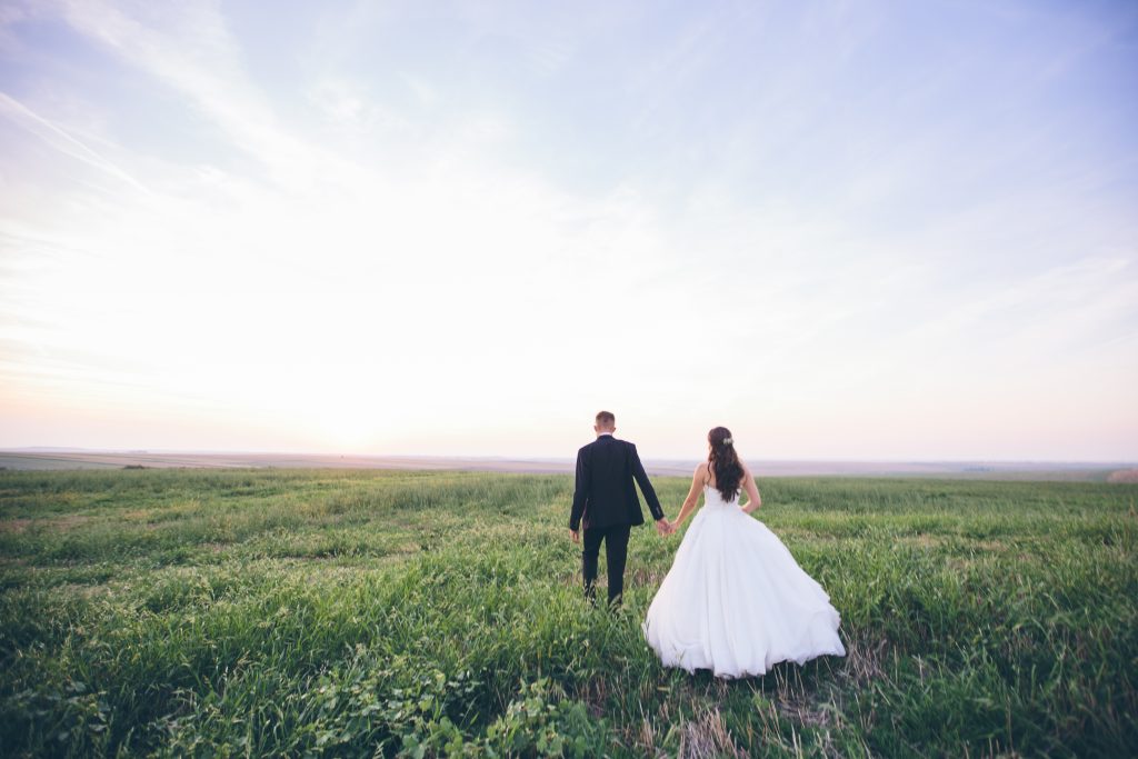 the bride and the groom walking in an open field