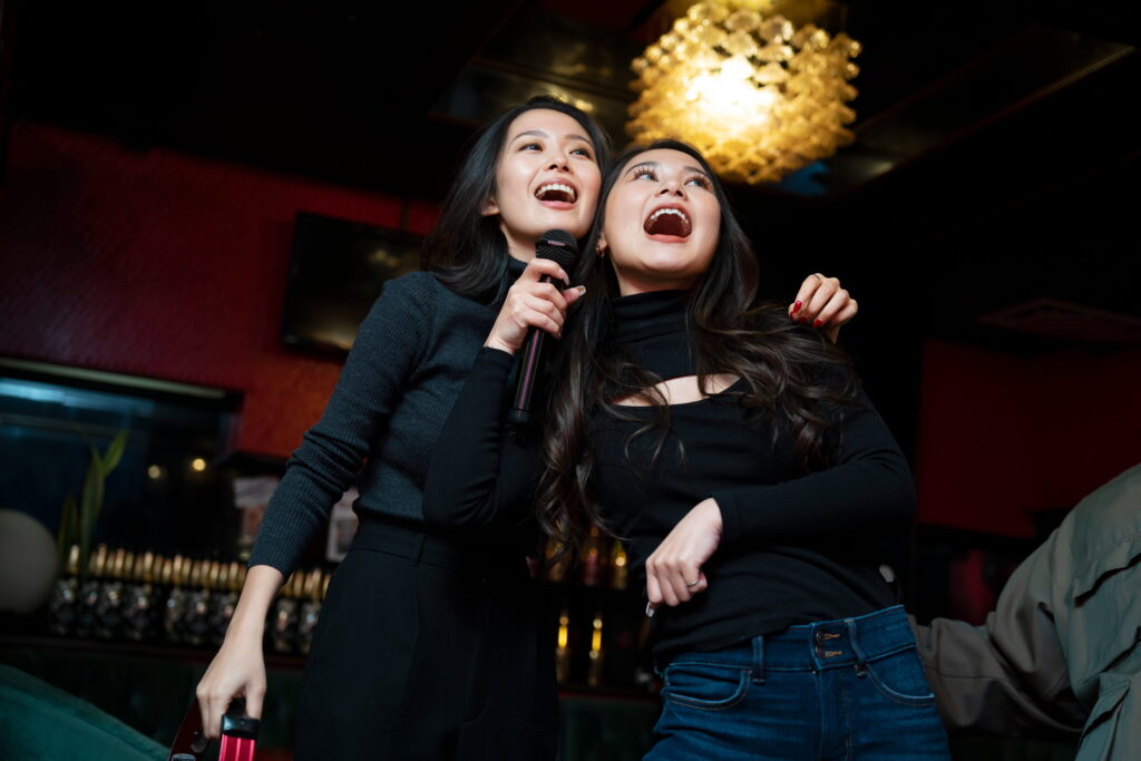Two women singing karaoke during a lively bachelorette party night with friends